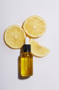 Beyaz arka planda limon dilimleri olan kozmetik yağı şişesinin üst görüntüsü
