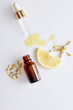 Kozmetik yağının şişenin yanından akışını beyaz arka planda limon dilimi ve vanilya tomurcukları    