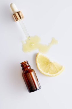 Top view of cosmetic oil flowing out of dropper next to bottle and slice of lemon on white background clipart