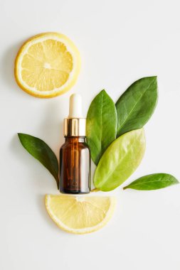 Beyaz arka planda yaprakları ve limon dilimleri olan bir şişe kozmetik yağı.