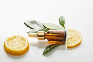 Beyaz arka planda yaprakları ve limon dilimleri olan kozmetik yağı şişesinin üst görüntüsü, panoramik çekim 