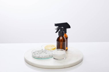 Şişeler dolusu yağ, kozmetik krem ve dekoratif boncuklu laboratuvar bardakları, gri üzerine izole edilmiş bir dilim limon.