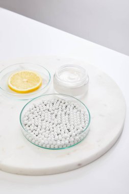 Dekoratif boncuklu laboratuvar vitrinleri ve kozmetik kremin yanında bir dilim limon gri bölmede izole edilmiş.