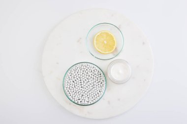 Dekoratif boncuklu laboratuvar vitrininin üst görüntüsü, beyaz arka planda kozmetik kremin yanında bir dilim limon.