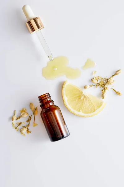ボトルの横のドロッパーから流れ出す化粧品油のトップビュー 白い背景にレモンとバニラの芽のスライス — ストック写真