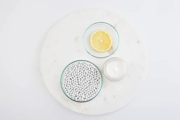 实验室玻璃器皿顶部 装饰有珠子 在白色底座上的化妆品奶油旁边有一片柠檬 — 图库照片