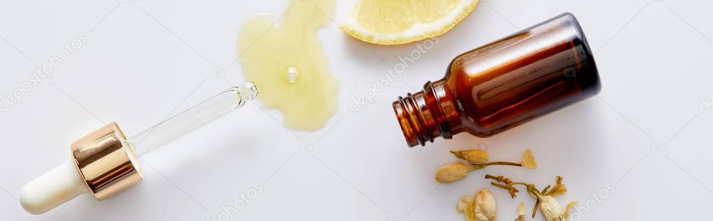 Top view of cosmetic oil flowing out of dropper next to bottle, slice of lemon and vanilla buds on white background, panoramic shot