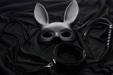 Siyah tekstil arka planında tavşan maskesi ve seks oyuncakları