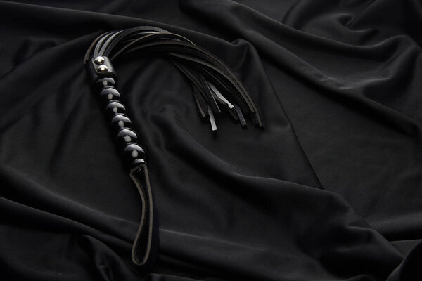 leather flogging whip on black textile background