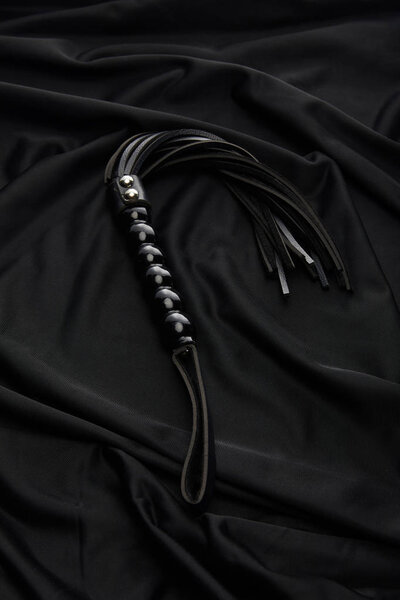leather flogging whip on black textile background