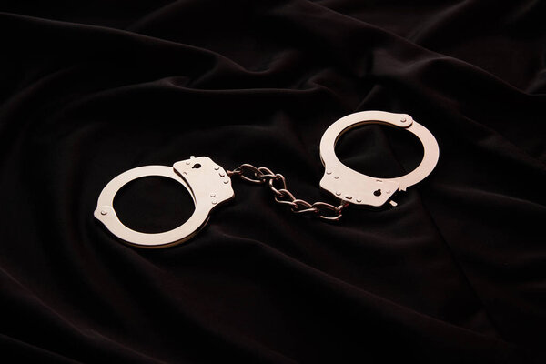 металлические наручники на черном текстильном фоне
