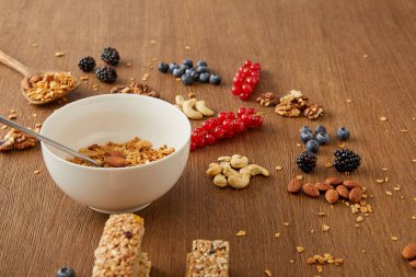 Tahta arka planda böğürtlen, fındık ve mısır gevreği barlarının yanında granola ile kase