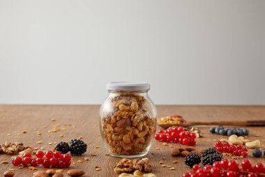 Selective focus of jar of granola with nuts, oat flakes, berries and cereal bars on wooden background isolated on grey clipart