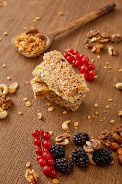 Selective focus of cereal bars, spatula with granola, redcurrants, blackberries and nuts on wooden background clipart