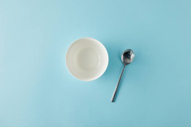Mavi arka planda boş kase ve kaşığın üst görünümü
