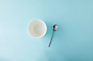 Top view of empty bowl and teaspoon on blue background clipart