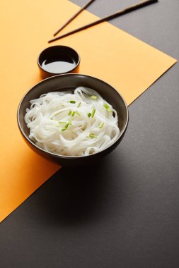 rice noodles in bowl near chopsticks and soy sauce on yellow and black surface clipart