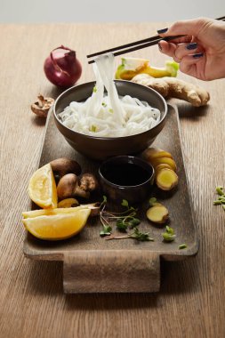 Tahta tepside zencefil kökü, limon ve sebzeli pirinç eriştesi yiyen bir kadın.