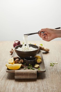 Zencefil kökü, limon ve sebzeli pirinç eriştesi yiyen bir kadının gri tepside izole edilmiş ahşap tepsisi.