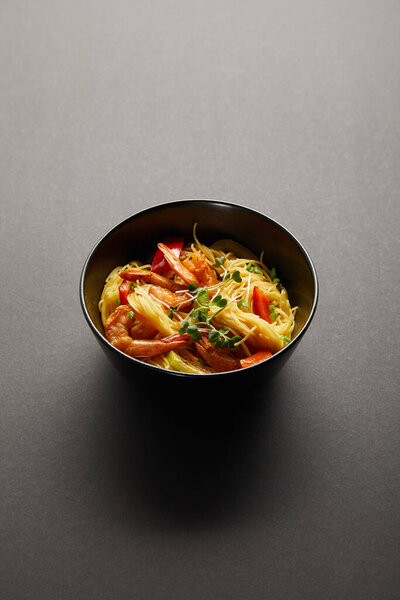 noodles with shrimps and vegetables in bowl on black background