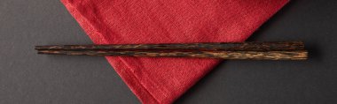 top view of wooden chopsticks on red napkin on black background, panoramic shot clipart