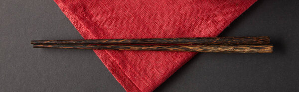 top view of wooden chopsticks on red napkin on black background, panoramic shot