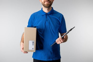 Cropped view delivery man holding cardboard box and clipboard isolated on grey clipart