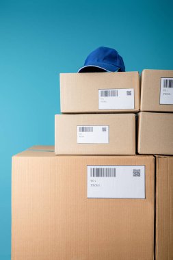 Cap on stacked cardboard boxes with qr and barecodes isolated on blue clipart
