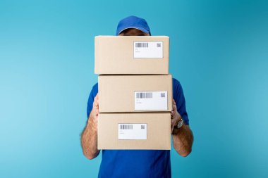 Delivery man holding cardboard packages with qr codes and barcodes isolated on blue clipart