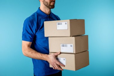 Cropped view of delivery man holding cardboard packages isolated on blue clipart