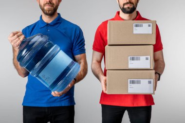 Gri üzerinde karton paketler ve şişe su taşıyan kuryelerin kırpılmış görüntüsü