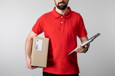 Kırpılmış sakallı kurye görüntüsü Gri üzerinde izole edilmiş pano ve karton paket tutuyor