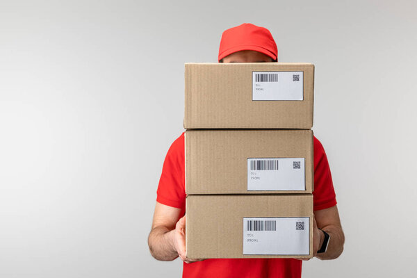 Delivery man in uniform holding cardboard boxes isolated on grey