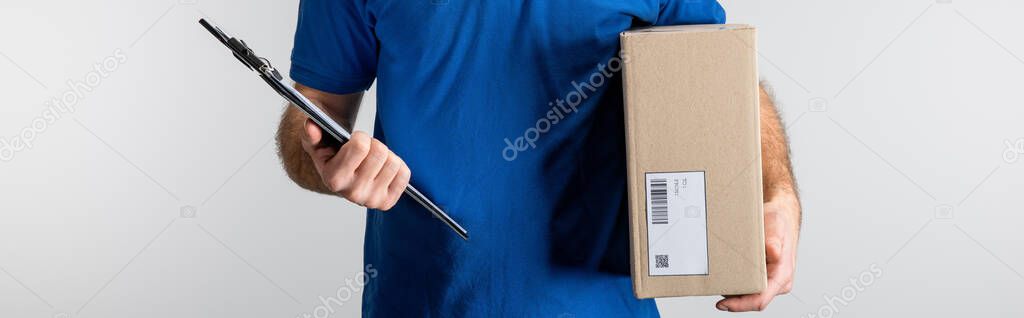 Panoramic shot of courier holding clipboard and cardboard box isolated on grey