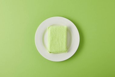 top view of white plate and sponge for dish washing on green