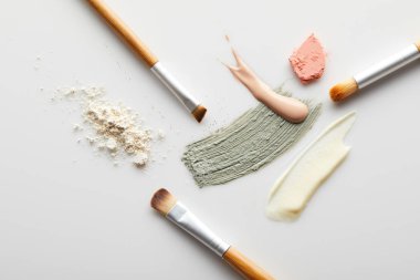 Yüz pudrası, kil, kozmetik ve ton kremi fırça darbeleri, fırçalar ve gri arka planda kızartıcı