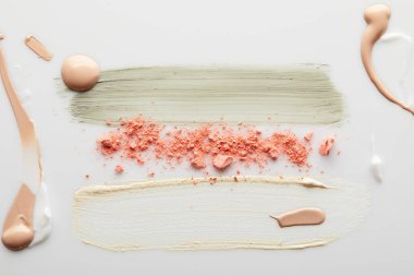 Kozmetik ve ton kreminin üst görüntüsü, gri arkaplanda pembe allık ile kil fırça darbeleri