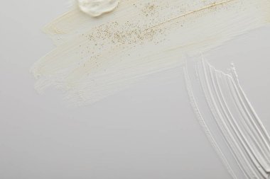 Ton ve kozmetik kremin üst görüntüsü ve gri arka planda jel ve altın parıltılı kil fırça darbeleri