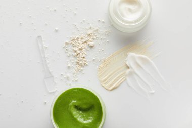 Ovalama ve kozmetik kremi, fırça darbeleri, yüz pudrası ve gri arka planda spatula içeren konteynırların üst görüntüsü