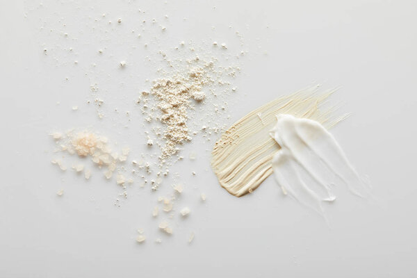 Top view of sea salt, face powder, cosmetic and tone cream brushstrokes on grey background