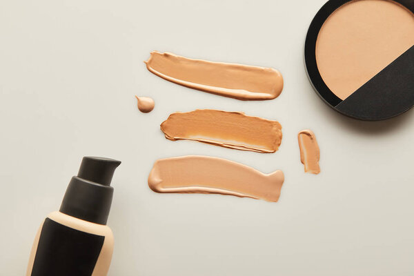 Вид сверху дозатора, тональные кремовые брюшки с порошком для лица на сером фоне
