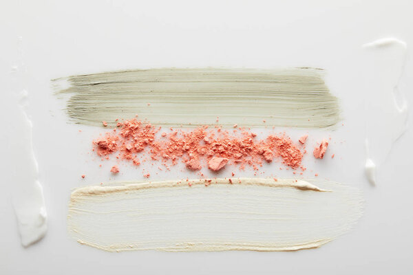 Вид сверху на косметический и тональный крем, когтистые брюшки с блушером на сером фоне
