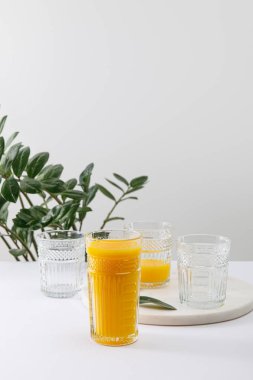 Beyaz yüzeyde, yeşil bitkinin yakınında, gri üzerine izole edilmiş lezzetli sarı smoothie.