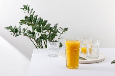 Yeşil bitkinin yanındaki beyaz yüzeyde lezzetli sarı smoothie.