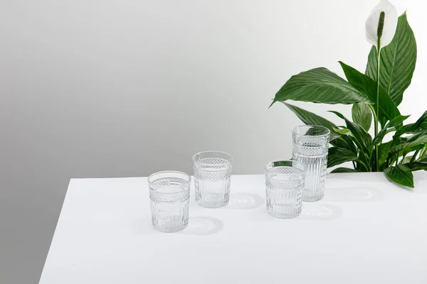 緑の平和ユリの花の近くの白いテーブルの上に新鮮な水のファセットグラス — ストック写真