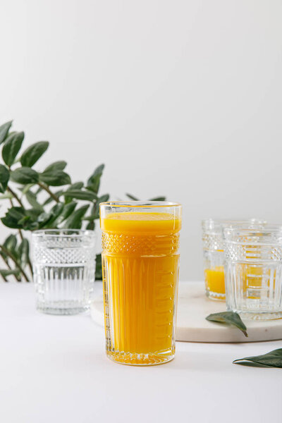 selective focus of glass of delicious yellow smoothie on white surface near green plant isolated on grey