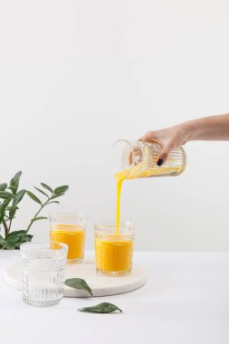 Kırpılmış bir kadın manzarası var. Lezzetli sarı smoothie bardağa dökülüyor. Yeşil bitkinin yanında.