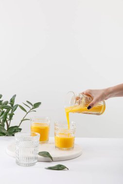 Kırpılmış bir kadın manzarası var. Lezzetli sarı smoothie bardağa dökülüyor. Yeşil bitkinin yanında.