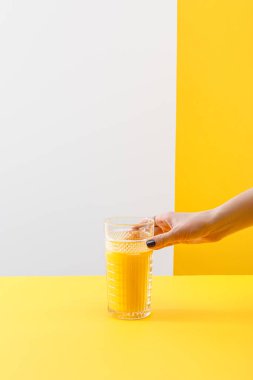 Gri ve sarı arka planda taze, lezzetli sarı smoothie bardağı tutan bir kadın görüntüsü.