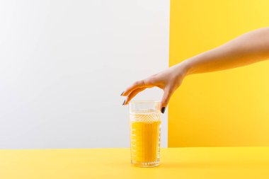 Gri ve sarı arka planda taze, lezzetli sarı smoothie bardağı tutan bir kadın görüntüsü.